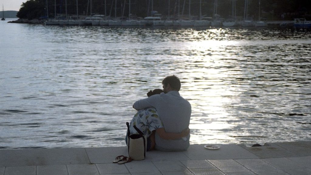 boy in white shirt sitting on brown floor tiles near body of water during daytime