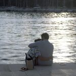 boy in white shirt sitting on brown floor tiles near body of water during daytime