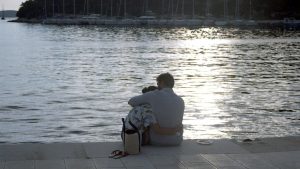 boy in white shirt sitting on brown floor tiles near body of water during daytime